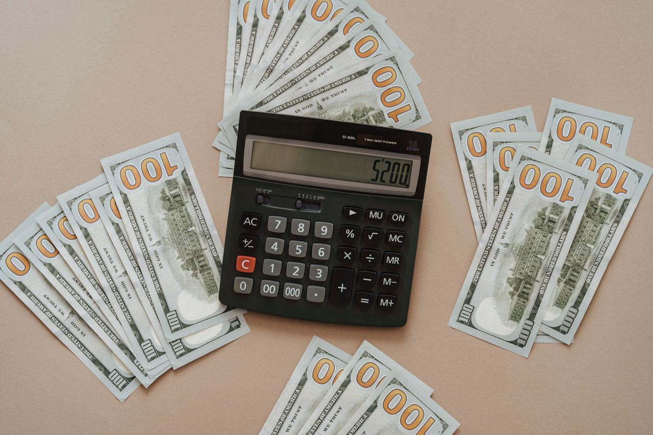Calculadora ao lado de cédulas de dinheiro sobre uma mesa, representando o cálculo dos juros acumulados no cartão de crédito