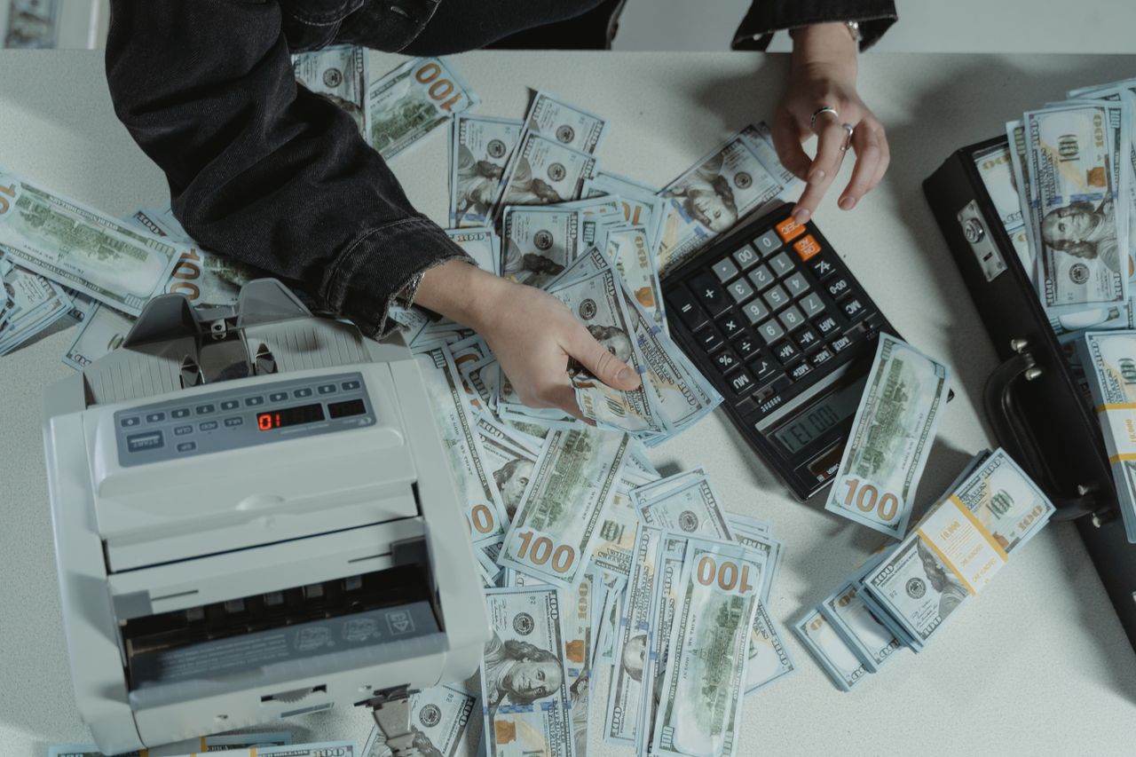 Mão segurando cédulas de dinheiro ao lado de uma calculadora, representando o cálculo do impacto da inflação no orçamento